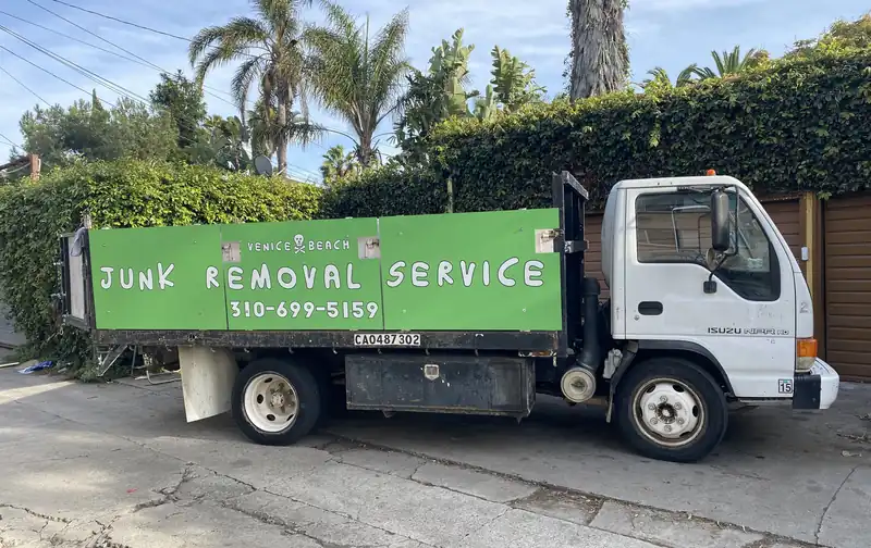Venice Beach Junk Removal truck with its green junk removal service sign, parked in a Venice alley