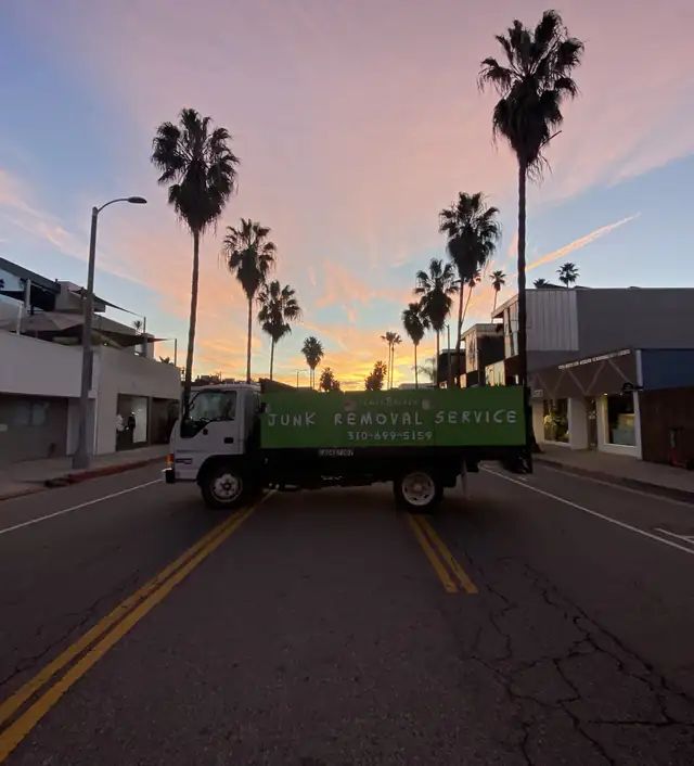 The green Venice Beach Junk Removal truck on a Venice street at sunset, under the palm trees